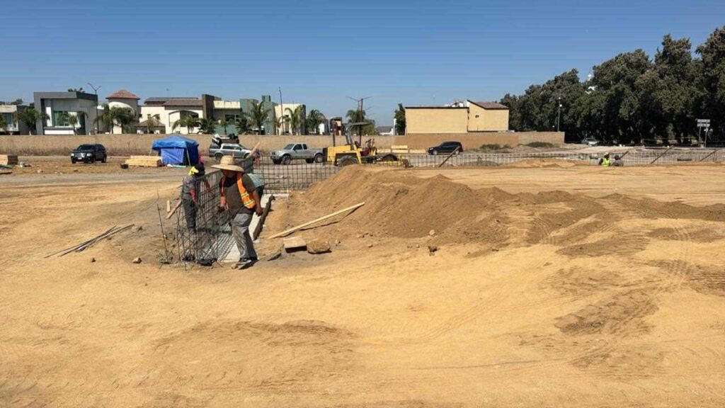 Trabajadores de construcción preparando estructuras de refuerzo en un terreno amplio bajo un cielo despejado en un entorno urbano.